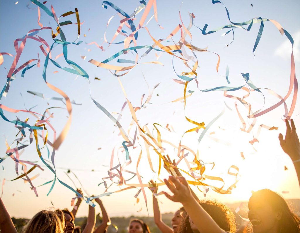 crowd at an outdoor party bursting colorful streamer confetti